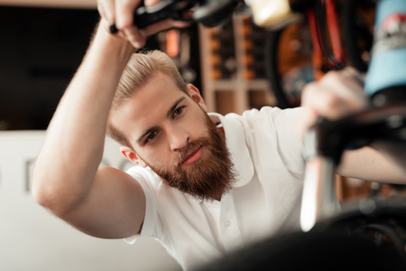 A young man with a beard looks at the details of the bicycle in the bicycle store.の写真素材