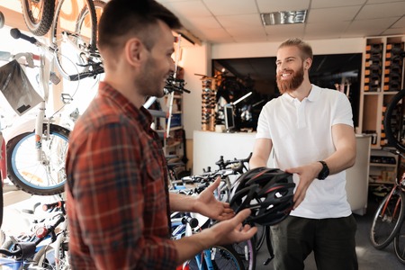 The man-seller shows the buyer a helmet for bike rides.の写真素材