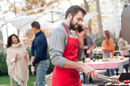 A man is cooking sausages on the grill, talking on the phone.の写真素材