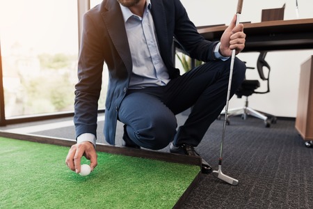 Close up. A man in a business suit plays golf in the officeの写真素材