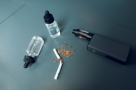 Electronic cigarette - boxmod, liquid for vape and a broken cigarette lie on the table.