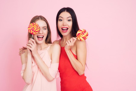 Two girls with lollypops on pink background celebrating womens day March 8.の写真素材