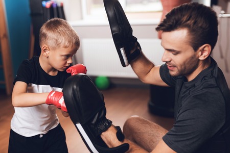 Father and son in the gym. Father and son spend time together and lead a healthy lifestyle. The father teaches his son to box. Boy in boxing gloves.の写真素材