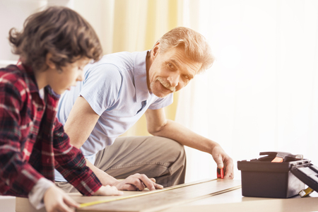 Good time together. Grandfather and grandson are measuring a table with measuring tape.の写真素材