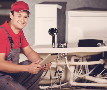 Plumber standing in front of washbasin writing on clipboard.