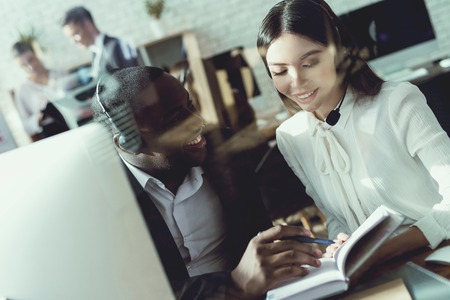Black guy and Asian girl communicate in the call center. They work as operators. They are in a good mood.の写真素材
