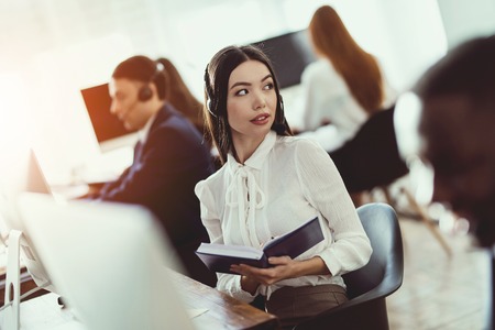The Asian girl answers questions from clients in the call center. People from different...
