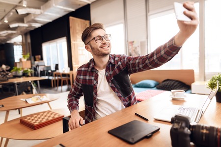 Freelancer man wearing shirt and glasses taking selfie at laptop sitting at desk.の写真素材