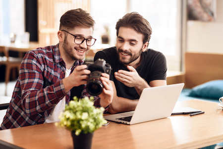 Two freelancer men in shirt and t-shirt looking at photos at laptop at desk.の写真素材