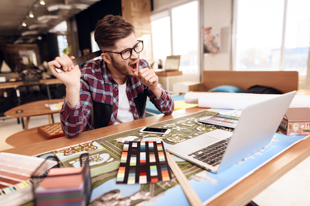 Freelancer man in shirt yawning at laptop sitting at desk.の写真素材