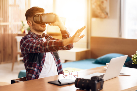 Freelancer man using wearing shirt and glasses virtual reality at laptop sitting at desk.