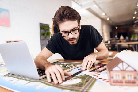Freelancer bearded man in t-shirt using ruler at laptop sitting at desk.