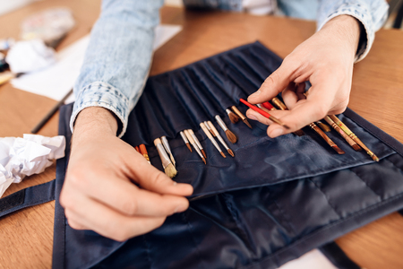Close up freelancer man in jeans shirt taking out brushes sitting at desk.の写真素材