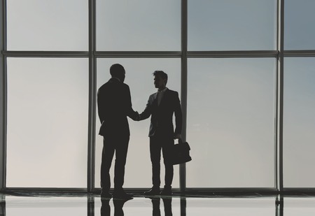 Silhouette view of two young businessmen are standing in modern office with panoramic windows.の写真素材