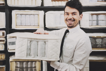 The young salesman is showing quality mattresses in the store.の写真素材