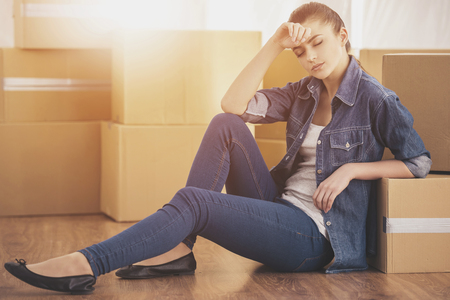 The young happy woman sits in a room near boxes. Moving, purchase of new habitation.の写真素材
