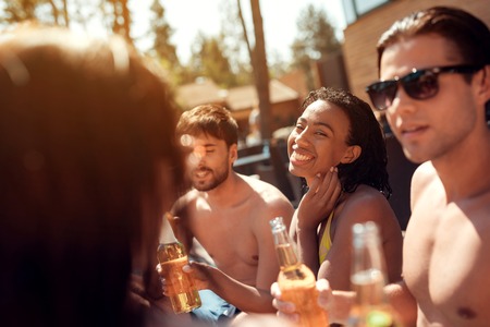 Happy friends cheering with beer bottles in swimming pool. Swimming pool party. Company of young people spend weekend in pool.の写真素材