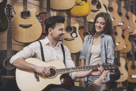 Man is playing guitar near young girl on a background of guitars in the music store.の写真素材