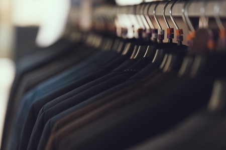 Close up. Business mens suits hang on hangers in boutique of business clothes. Big choice of suit. Wardrobe. Dressing room.