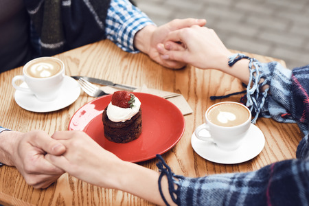 Close up. Cheesecake on table in cafe. Couple holding handsの写真素材