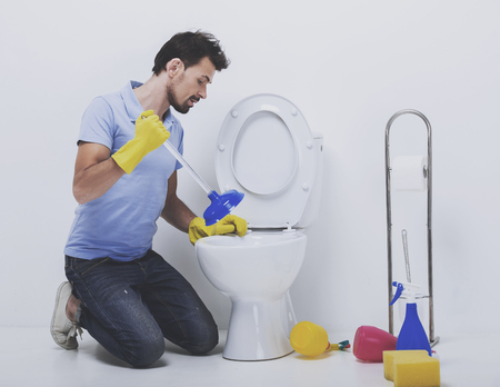 Young man unclogging toilet with plunger. Plumber sits next to wc.の写真素材