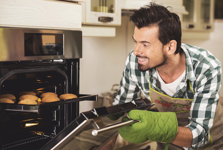 Portrait of smiling man holding tray of bakes in kitchen at home. Delicious cookies.の写真素材