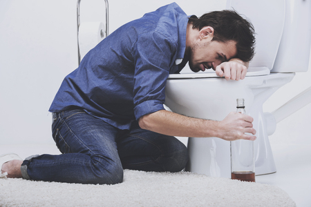 Man sit near toilet with bottle. Man vomits in toilet. Concept after drinking.の写真素材