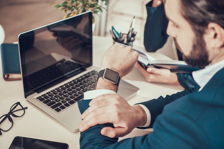 Worker in suit looking at watch at desk in office.