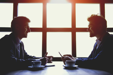 Two Businessmen Have Business Lunch with Cups of Coffee in Cafe. Business Concepts. Discussion of Financial Successes at Meeting in Modern Cafe with Coffee. Successful Partnership Concepts.の写真素材