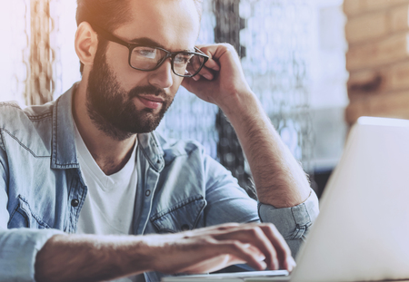 Handsome Successful Businessman in Casual Wear and New Eyeglasses Using Laptop. Pretty Man Working in Modern Office. Unrecognizable Guy Using Modern Portable Computer on Indoor Table.の写真素材