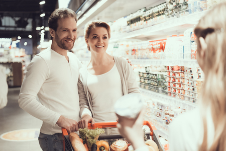 Family in Supermarket in Dairy Department. Family with Shopping Trolley. Girl near Shelf. Shelf with Milk Products. Consumerism Concept. Man in Shirt. Shopping in Supermarket. Family Concept.の写真素材