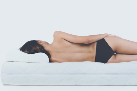 Young Bare Woman Lying on Orthopedic Mattress. Isolated on White Background. Healthy Concept.の写真素材
