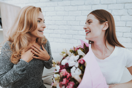 Smiling Daughter Gives Mother Flowers and Gift. Relationship in Family. Holiday at Home. Happy Mother. Friendly Relations. Celebrating Together. Happiness in Family Concept. Presenting Gift.の写真素材