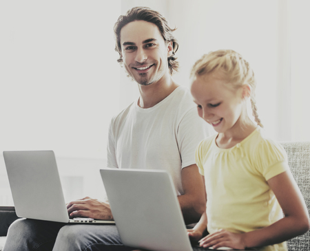 Handsome Father and Little Daughter Using Laptops and Smiling while Sitting on Couch at Home. Single...