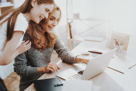 Mother and Daughter Watching into Laptop at Home. Daughter Helping Mother. Mother and Daughter at Home. Teenage Girl. Frilancing Mother Concept. Women Using Digital Device. Smiling Woman.の写真素材