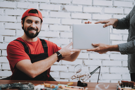 Worker Giving to Man Fixed Laptop in Workshop. Modern Workshop Concept. Manufacturing Instrument. Modern Tools Concept. Electronic Devices Concept. Mobile Device Hardware. Wooden Desk.の写真素材