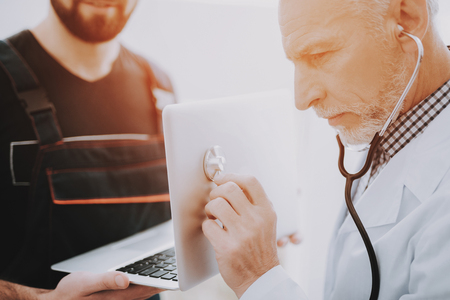 Computer Doctor in White Uniform with Stethoscope. Young Man with Laptop. Examination of Didital Device. Modern Devices. Digital Device. Electronic Devices Concept. Diagnostic Tool.の写真素材