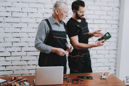 Workers Checking Device in Hands in Repair Shop. Worker with Tools. Computer Hardware. Young and Old Workers. Modern Devices. Digital Device. Wooden Table. Electronic Devices Concept.の写真素材