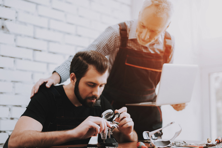 Two Men Repairing Hardware Equipment in Workshop. Repair Shop. Worker with Tools. Computer Hardware. Young and Old Workers. Modern Devices. Digital Device. Laptop on Desk. Electronic Devices Concept.の写真素材