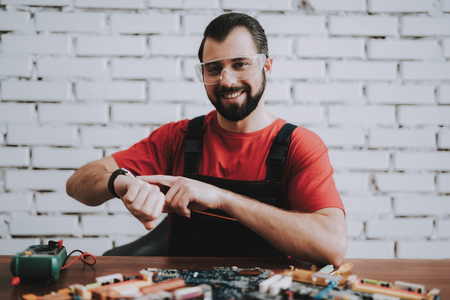 Young Man in Uniform with Broken Motherboards in Shop. Modern Workshop Concept. Manufacturing Instrument. Modern Tools Concept. Electronic Devices Concept. Mobile Device Hardware. Wooden Desk.の写真素材