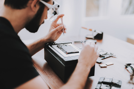 Young Man Repairing Hardware Equipment in Repair Shop. Worker with Tools. Computer Hardware. Electronic Devices Concept. Bearded Man. Modern Devices. Digital Device. Man in Glasses.の写真素材