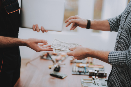 Worker Giving to Man Fixed Laptop in Workshop. Modern Workshop Concept. Manufacturing Instrument. Modern Tools Concept. Electronic Devices Concept. Mobile Device Hardware. Wooden Desk.の写真素材
