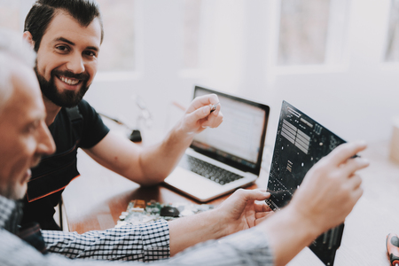 Two Men Repairing Hardware Equipment from Laptop. Repair Shop. Worker with Tools. Computer Hardware. Young and Old Workers. Digital Device. Laptop on Desk. Electronic Devices Concept.の写真素材