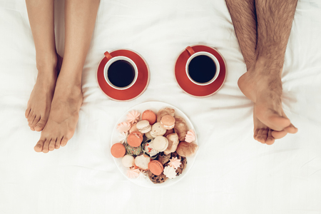 Happy Couple Are Lying In Bed At Valentine's Day. Tea And Plate Of Sweets Concept. Sweetheart's Holiday. Origami Roses. Celebrating Date. Young And Handsome. Pair Of Legs. Happy Together.の写真素材