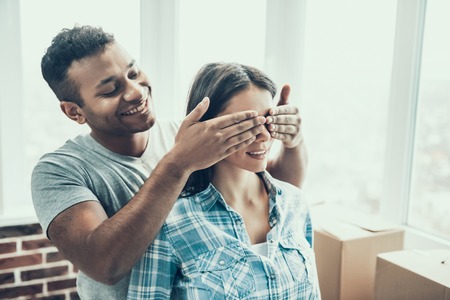 Young Smiling Couple Having Fun Moving in New Home. Beautiful Couple Enjoy playing Guess who game after Packing Cardboard Boxes in New Apartment. Relocation and House Moving Conceptの写真素材