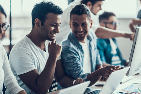 Young Smiling Business People Working on Laptops. Group of Young Coworkers Sitting Together at Table and Working on Laptops in Modern Office. Teamwork Concept. Corporate Lifestyleの写真素材