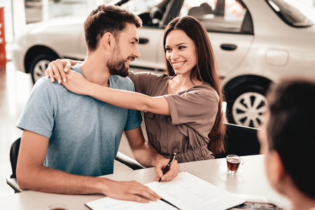 Happy Young Family Are Signing A Contract To Buy A Car. Dialogue With Dealer. Cheerful Customer. Automobile Salon. Make A Decision. Cup Of Coffee. End Of A Deal. Good Offer. Buyer And Seller.の写真素材