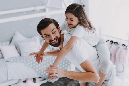 Cute Young Daughter on Piggy Back Ride with Dad. Happy Father's Day Concept. Father with Daughter Spending Time Togetherness at Home. Happy Family Daughter Laughs on Holidayの写真素材