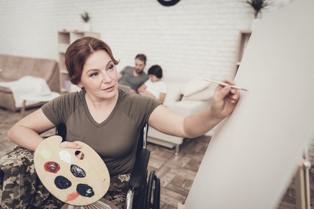 Disabled Soldier In Wheelchair Draws A Picture. After War Concept. Camouflage Uniform. Paralyzed Woman With Tassel. Home Leisure. Return From Army. Family Background. Husband And Son.の写真素材
