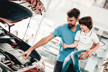 Young Family Are Choosing A New Car In Showroom. Automobile Salon. Father And Son. Good Mood. Make A Desicion. Auto Rewiew. Quality Control. Reliability Mark. Looking Under The Hood.の写真素材